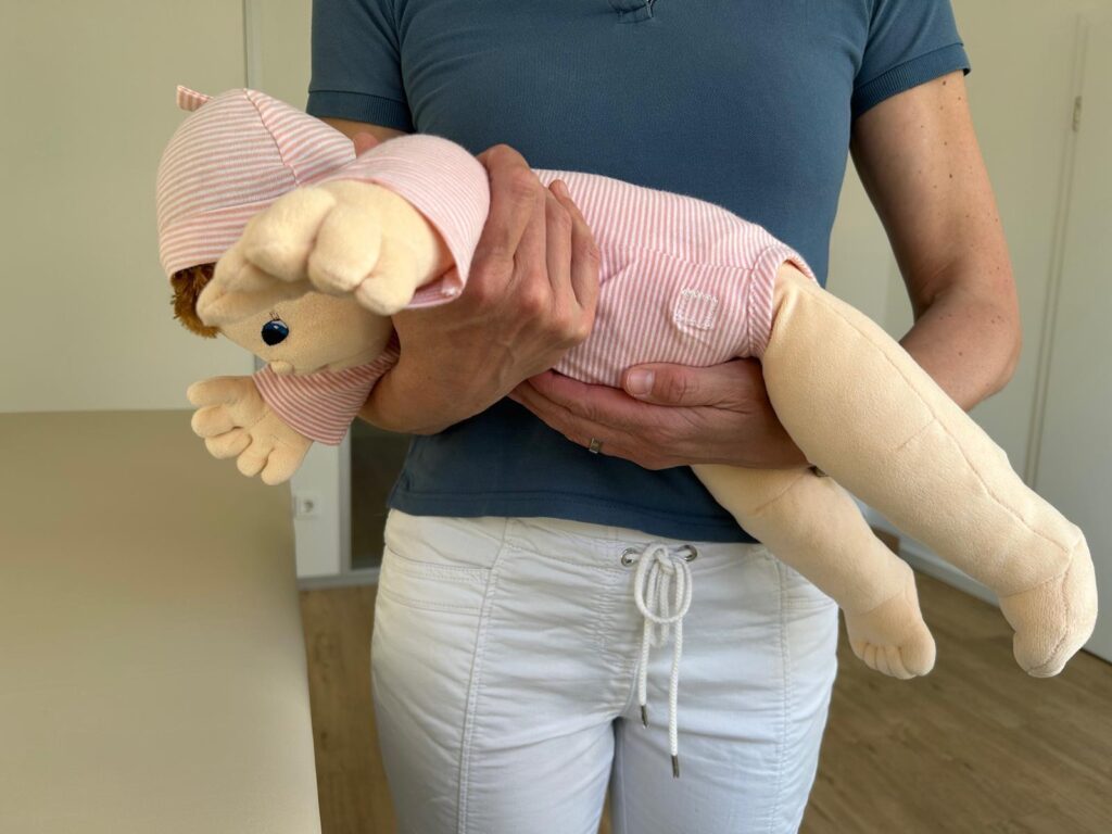 Fliegergriff in Bauchlage zur Linderung von Blähungen – sichere Trageposition für Neugeborene, demonstriert in der Kinderphysiotherapie Ritterburg