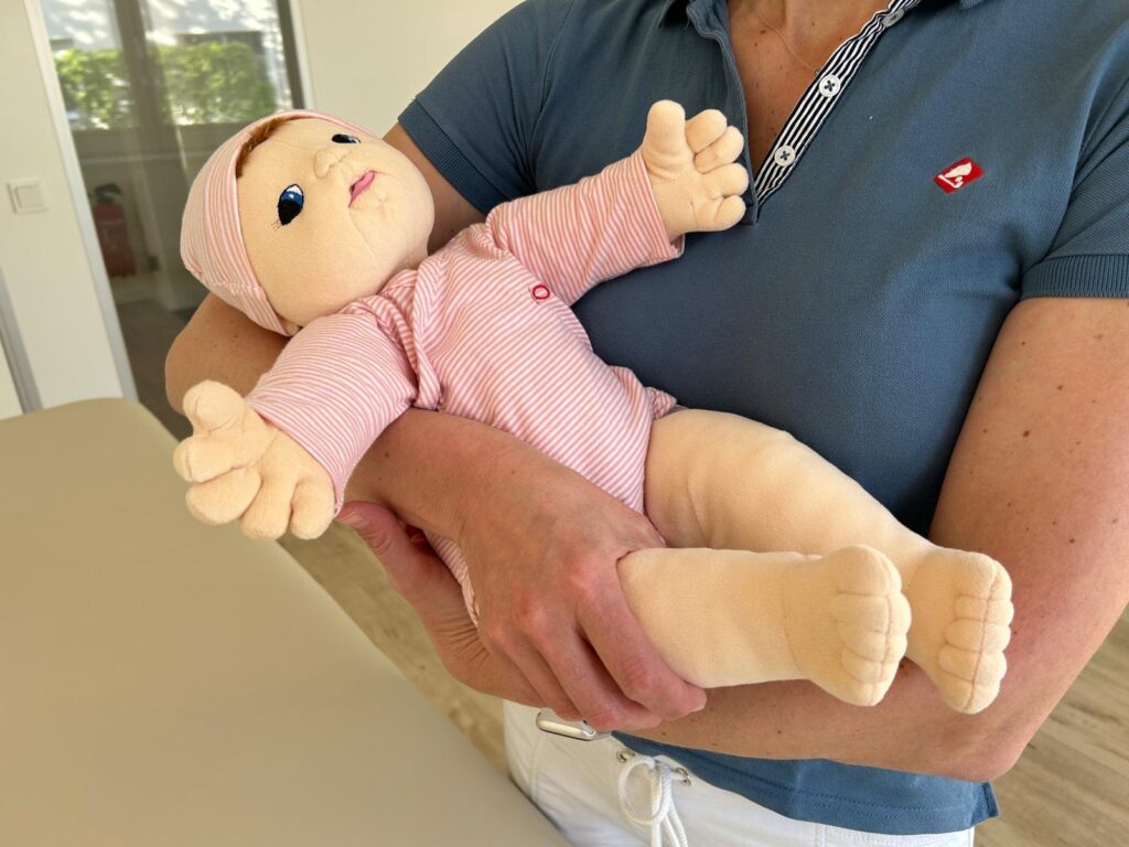 Sicheres Tragen eines Babys im Arm in seitlich gestützter Haltung – gezeigte Trageposition in der Kinderphysiotherapie Ritterburg