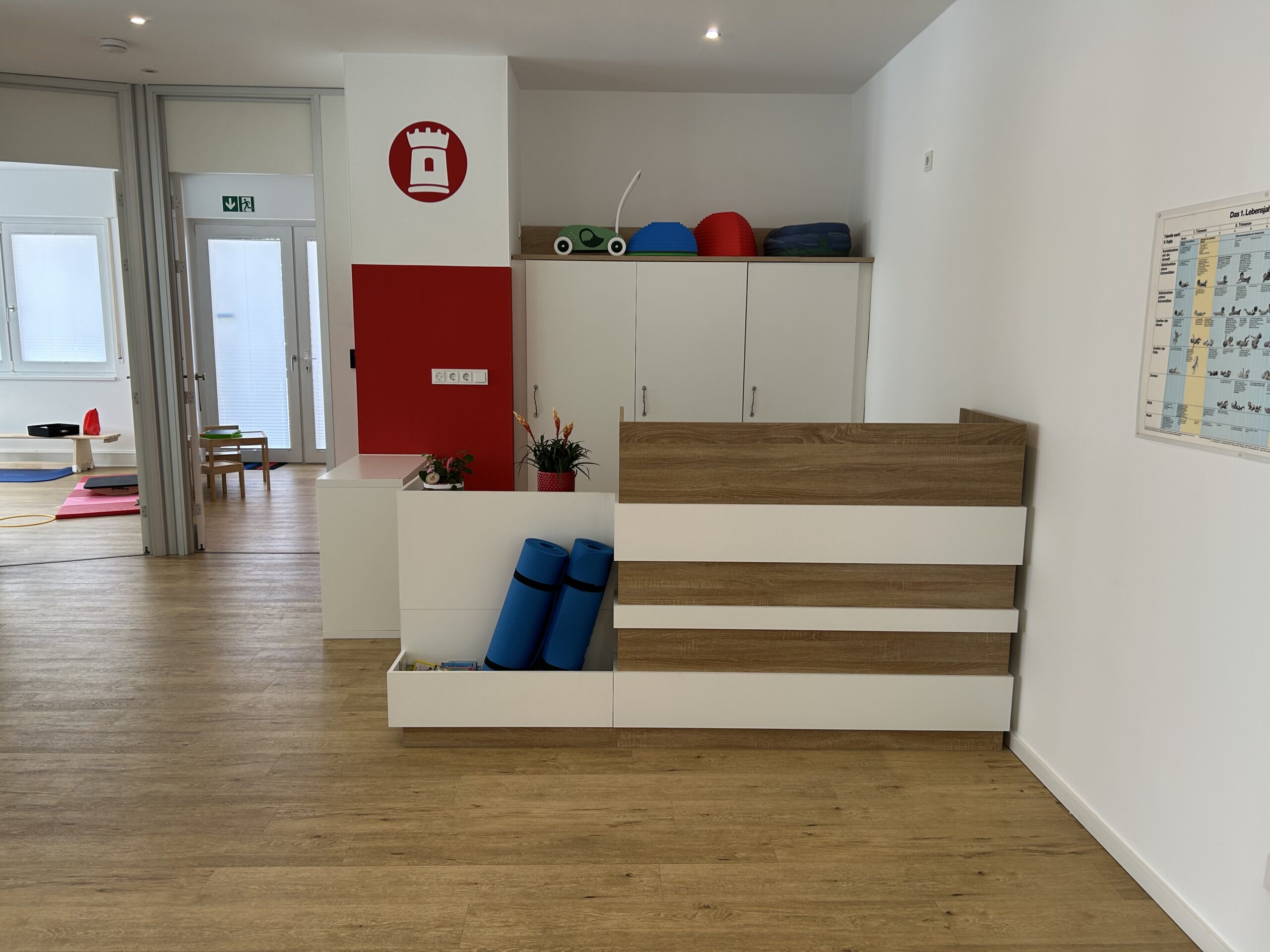 Empfangsbereich der Kinderphysiotherapie Ritterburg in Münster mit Matten, Therapiegeräten und rotem Logo mit Turm-Symbol