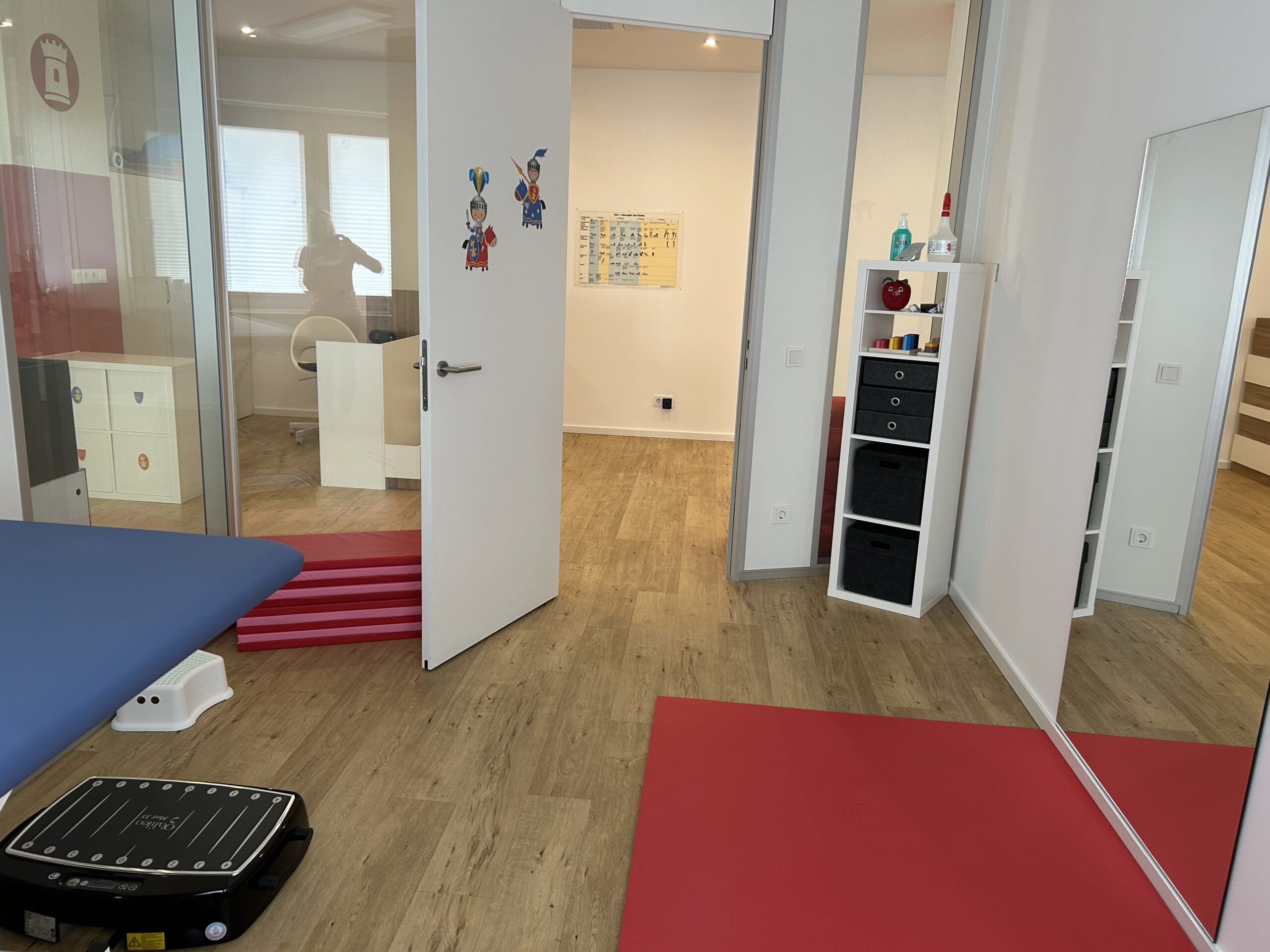 Behandlungsraum der Kinderphysiotherapie Ritterburg in Münster mit Therapieliege, Vibrationsplatte, Spiegelwand und kindgerechter Raumgestaltung